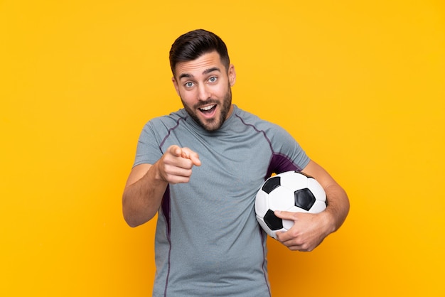 Football player man over isolated wall surprised and pointing front