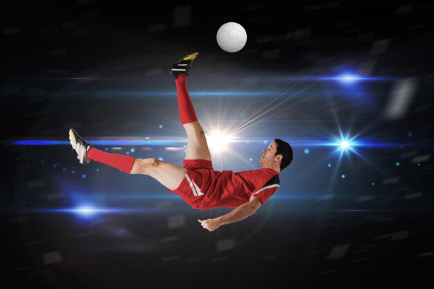 Football player in red kicking against black background with spark