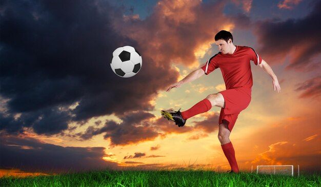 Футболист в красном пинает зеленую траву под голубым небом