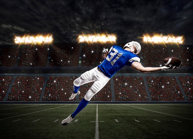 Photo football player with a blue uniform catching a ball on a stadium