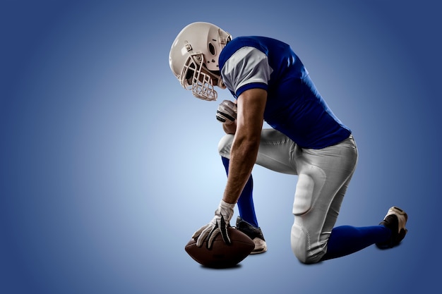 Football Player with a blue uniform on his knees on a blue wall