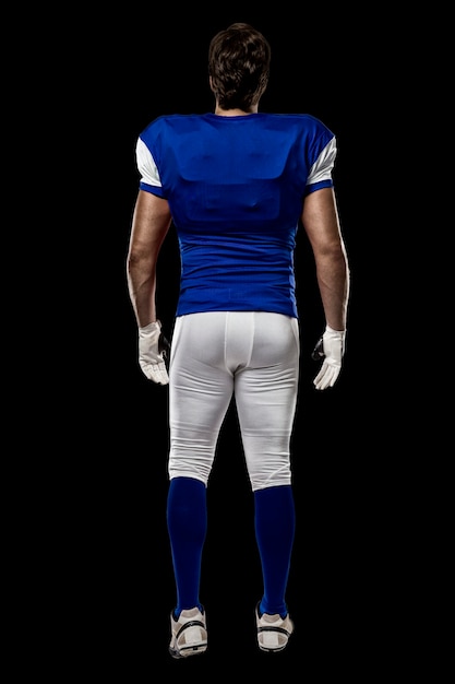 Football Player with a blue uniform walking, showing his back on a black wall