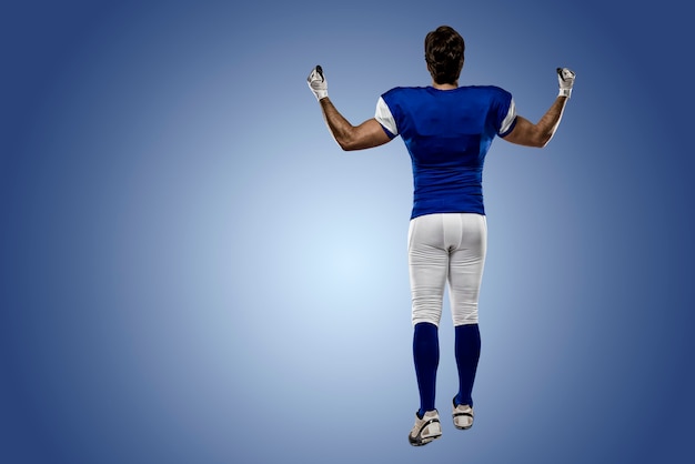 Foto giocatore di football americano con un'uniforme blu che cammina, mostrando la schiena su una parete blu