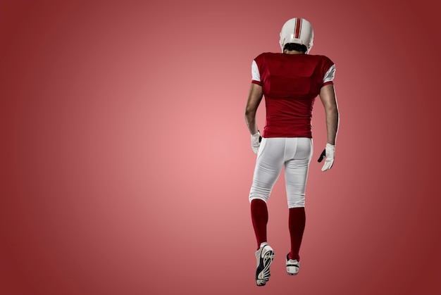 Football Player with a red uniform walking, showing his back on a red wall