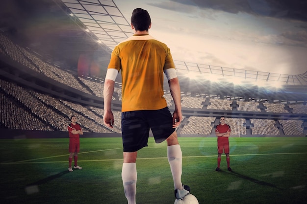 Футболист в желтом с мячом соперника против большого футбольного стадиона с огнями