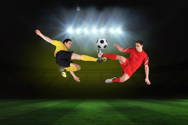 Football players tackling for the ball against football pitch under spotlights