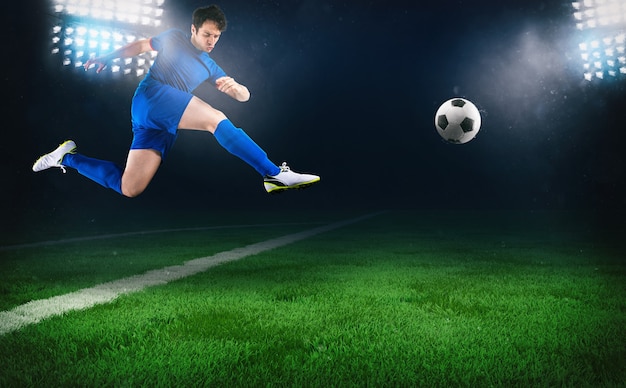 Football scene at night match with a soccer player running to kick the ball at the stadium