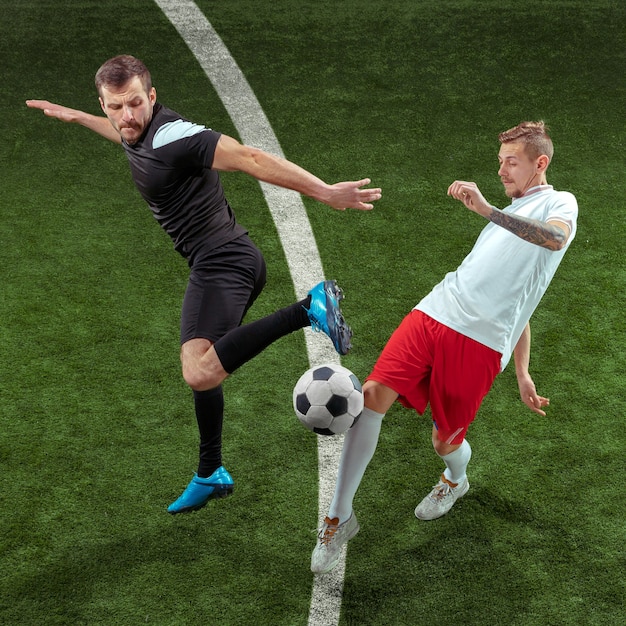 Football-speler aanpakken voor bal over groene gras achtergrond. Professionele mannelijke voetballers in beweging in het stadion. Fit springende mannen in actie, springen, beweging bij het spel.