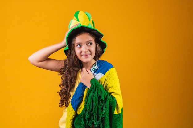 Football supporter, Brazil team. Beautiful little girl cheering for her team on yellow background