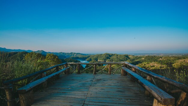 Footbridge leading towards mountains against clear blue sky