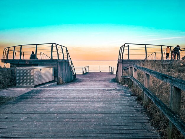 Footbridge over sea against sky during sunset