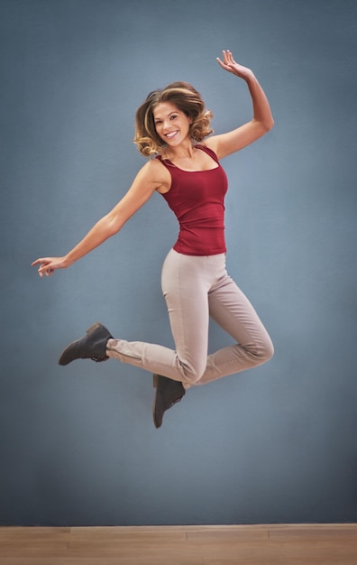 Footloose en fancy free Shot van een gelukkige jonge vrouw die in de lucht springt tegen een grijze achtergrond