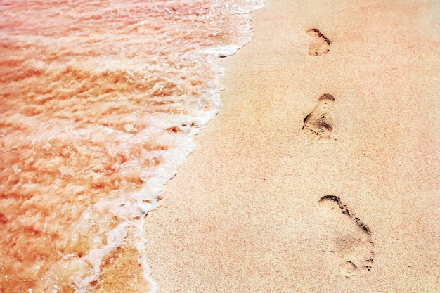 Impronte delle persone su una sabbia rosa dorata sulla costa del mare morbide onde di colore rosa sfondo creativo marino primo piano