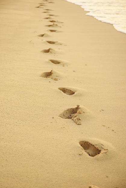 해질녘 모래에 발자국 바다 파도가 있는 아름다운 모래 열대 해변 해안의 발자취 계절 여름 배경