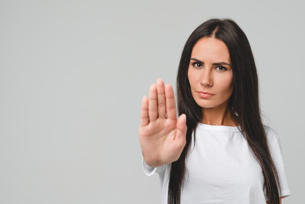 Forbidden prohibited serious caucasian young woman girl showing with palm hand stop sign gesture isolated in grey background No pass