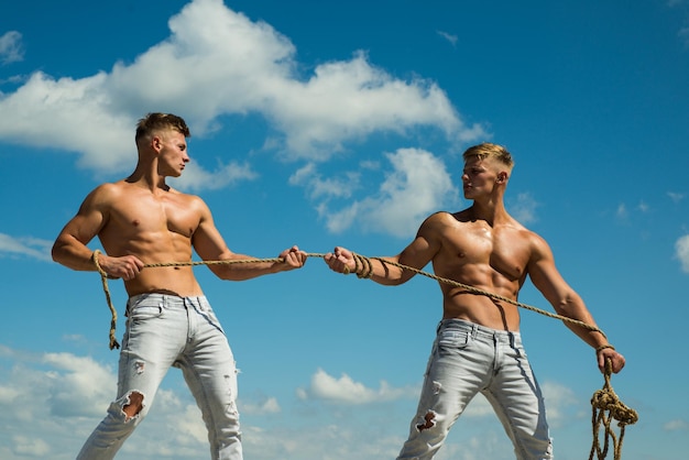 Photo force and power. twins competitors with muscular bodies. strong men pull rope with muscular hand strength. men shows off their strength against competitors. athletic twins on opposite sides