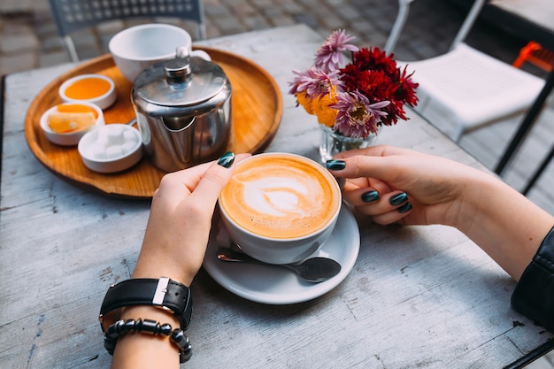 In the foreground a cup of coffee with foam a spoon and a plate\
tray with accessories for tea