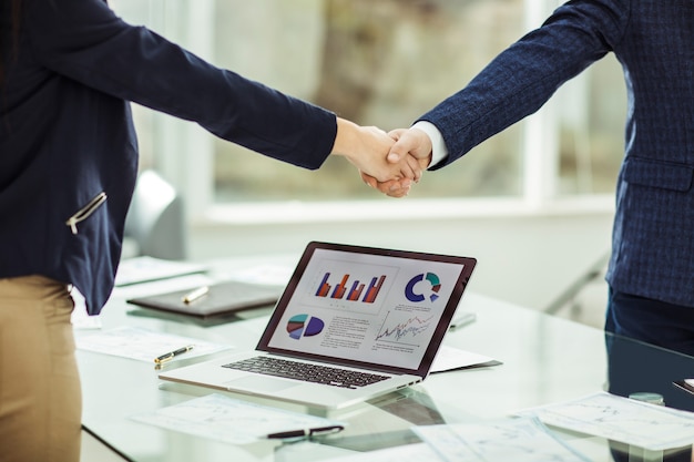 foreground is shaking hands with financial partners near the workplace in the modern office