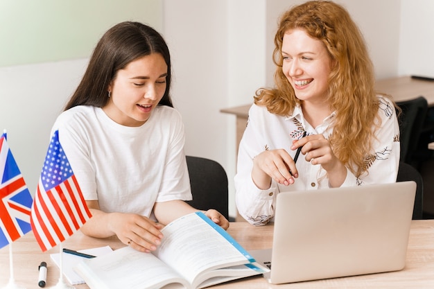 외국인 학교 개인 공부, 미소, 여고생과 웃음. 교사가 노트북을 사용하여 모국어 문법 설명