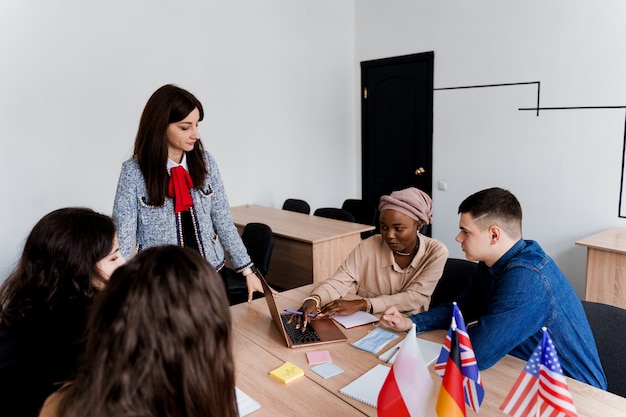 Foreign school private study with a school woman. Teacher explain grammar of native language using laptop. Prepearing to exam with tutor. English, British, German and Poland flags in front.