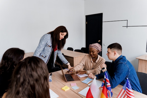 Foreign school private study with a school woman. Teacher explain grammar of native language using laptop. Prepearing to exam with tutor. English, British, German and Poland flags in front.