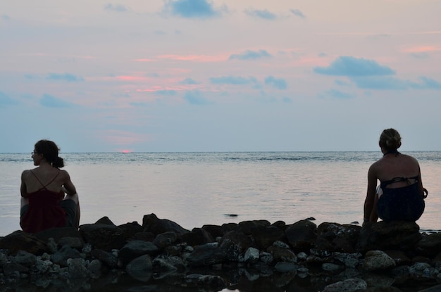 Le donne straniere e i viaggiatori di amici viaggiano visita e si siedono rilassati sulla ricreazione della spiaggia di roccia di pietra guardando l'oceano del mare nel golfo di thailandia mentre il tramonto al tramonto sull'isola di koh chang a trat thailandia