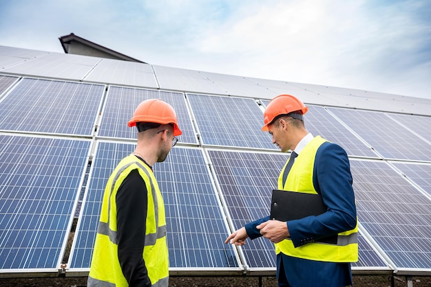 Foreman businessman in uniform and helmet tells the worker the plan on which to install solar panels Green electricity concept