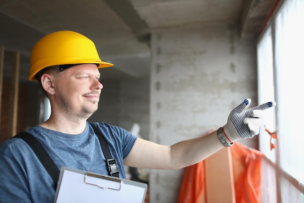 Foreman holding building plan and pointing outside window to look at business complex