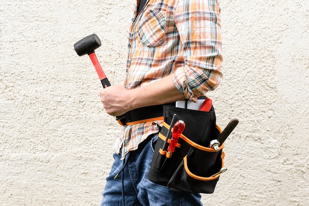 A foreman with a tool belt holds a rubber hammer.