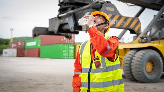 Foreman or worker is drinking a bottle of water after finishing\
work and relaxing on the old truck at cargo container port