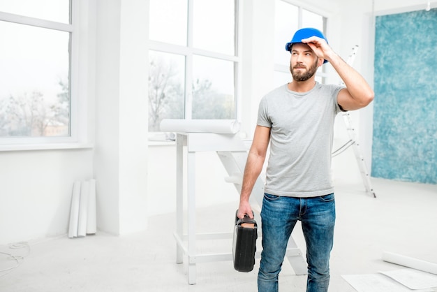 Foreman or worker in uniform with instruments standing in the white interior during the renovation