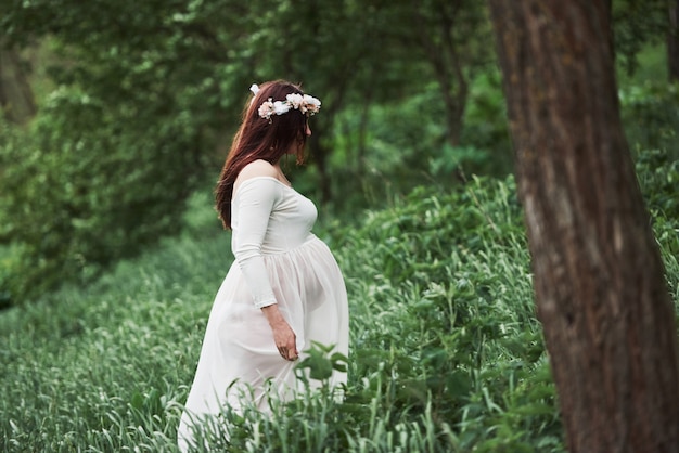 In the forest. Beautiful pregnant woman in dress have a walk outdoors. Positive brunette