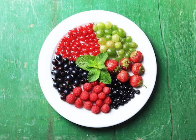 Лесные ягоды на тарелке, на цветной деревянной поверхности