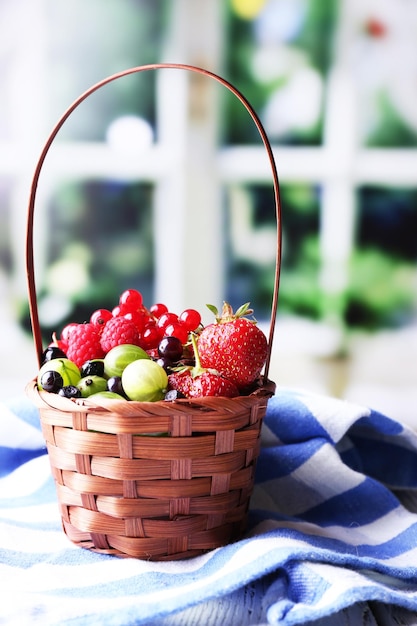 Forest berries in wicker basket on wooden table on bright background