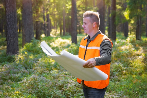 Forest engineer or surveyor holding maps and inspecting forest land