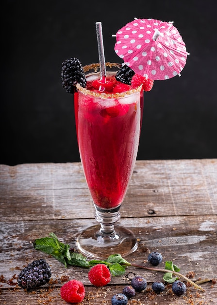 Forest fruit cocktail in a glass on a wooden base decorated with blackberries