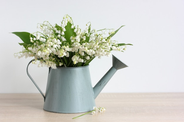 Forest lilies of the valley in a watering can on the table. a bouquet of white flowers.