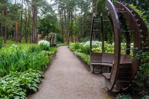 A forest park with large trees and creative benches and arches. 