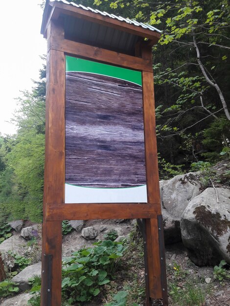 In the forest, there is a large wooden signboard with an empty space for insertion against a background of stones.