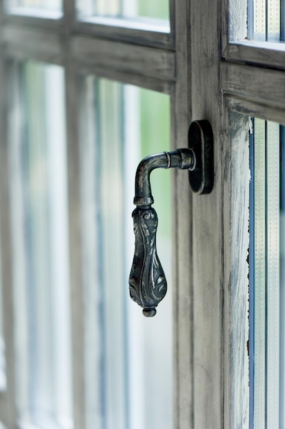 Forged handle on a lightcolored wooden windowClassical interior