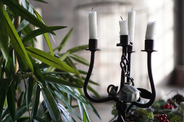 Forged metal candlestick with candles on blurred background with light from window