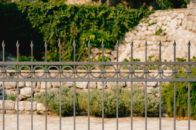 Foto recinzione in metallo forgiato con punte nella parte superiore di fronte a un edificio in pietra intrecciato con edera verde