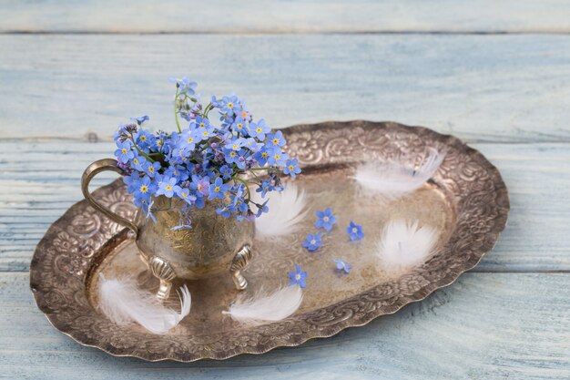 Forget me nots in a vase on an old silver tray and blue feathers