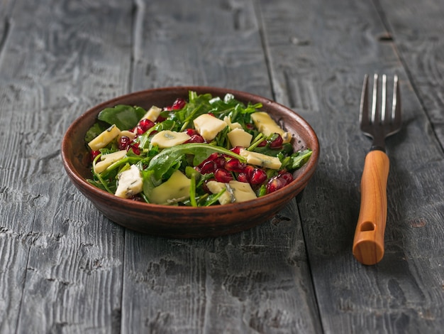 Fork and bowl with arugula, pomegranate and blue-mold cheese salad. Diet vegetarian salad.