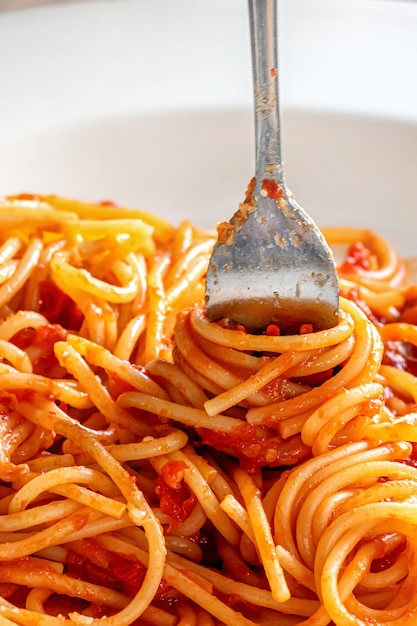 Fork close-up wrapped in Italian spaghetti pasta in white plate with ketchup sauce, vertical image