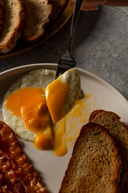 вилка деликатно разделяет золотой желток идеально жареного яйца на тарелке аппетитного вкусного завтрака
