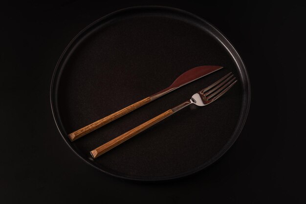 Forchetta e coltello su un piatto nero isolato su uno sfondo nero vista dall'alto
