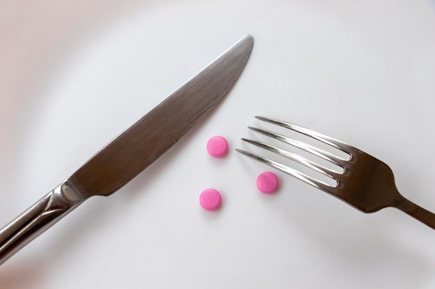 フォーク、ナイフ、丸薬がクローズアップで皿の上に横たわり、薬の使用のコンセプト