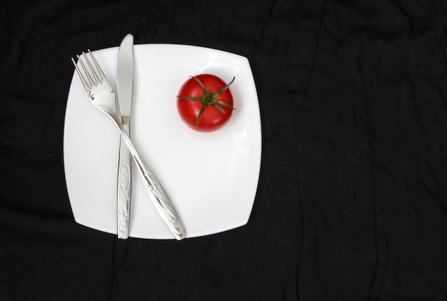 Fork knife and white plate with tomate over black background Clean plate and cutlery on background