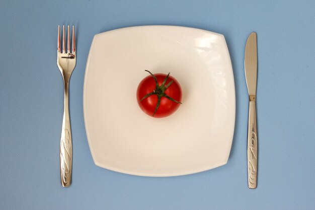 Foto coltello a forchetta e piatto bianco con pomodoro su sfondo blu piatto pulito e posate